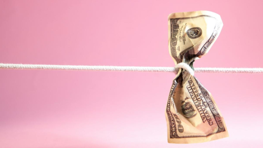 Auf rosa Hintergrund ein von einer Schnur umwickelter Dollarschein