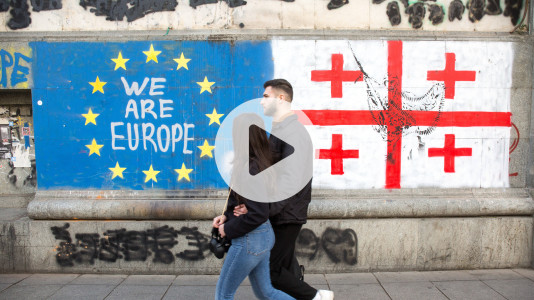 Foto: Zwei Personen gehen an einer Wand mit EU-Sternen, dem Schriftzug „Wir sind Europa“ (We are Europe) und der georgischen Flagge vorbei.