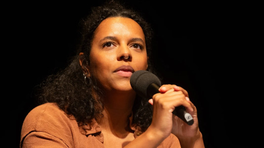 Alice Hasters mit einem Mikrofon in der Hand vor einem dunklen Hintergrund.