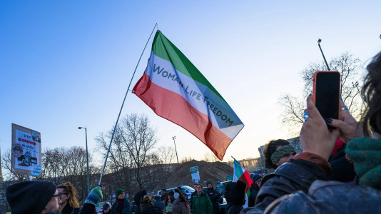 Eine grün-weiß-rote Flagge des Irans mit dem Schriftzug "Women Life Freedom"
